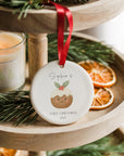 Personalised baby’s first Christmas pudding ornament hanging from a red ribbon on a wooden tiered tray, surrounded by dried orange slices and winter greenery