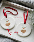 Two personalised baby’s first Christmas pudding ornaments with red ribbons showing custom name and date options, displayed on a white wooden tray with cosy winter textures