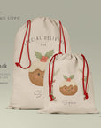 Side-by-side comparison of the large Christmas pudding Santa Sack and the smaller pudding Gift Sack presented on a sage green background. Both sacks showcase the illustrated pudding design with holly and festive details, printed on premium linen-style fabric with red drawcord ties. Text highlights available sizes, approximate measurements, and suggested uses such as Santa deliveries, toy storage, and reusable gift wrapping