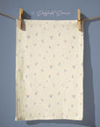 Warm butter-yellow tea towel patterned with tiny pastel floral motifs in soft pink and powder blue, spaced evenly for a light, airy spring cottage feel.