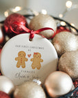 A personalised ceramic Christmas ornament showing a gingerbread couple with a red heart and the text “Our First Christmas as Fiancés” along with the names Olivia and Jack. The ornament is displayed in a basket filled with glittery red and gold baubles and soft fairy lights for a cosy, festive look