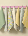 Pastel spring floral tea towel collection hanging on pink wall hooks featuring sage green, soft yellow and cottage garden prints in daffodil, blossom and stripe patterns for a country kitchen