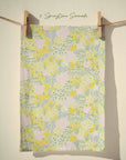 Pastel floral tea towel featuring yellow daffodils, blush pink blossom and sage green foliage in an all over country garden spring print