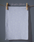 Powder blue tea towel with tiny scattered white floral details, minimalist cottagecore kitchen textile inspired by early spring blooms.