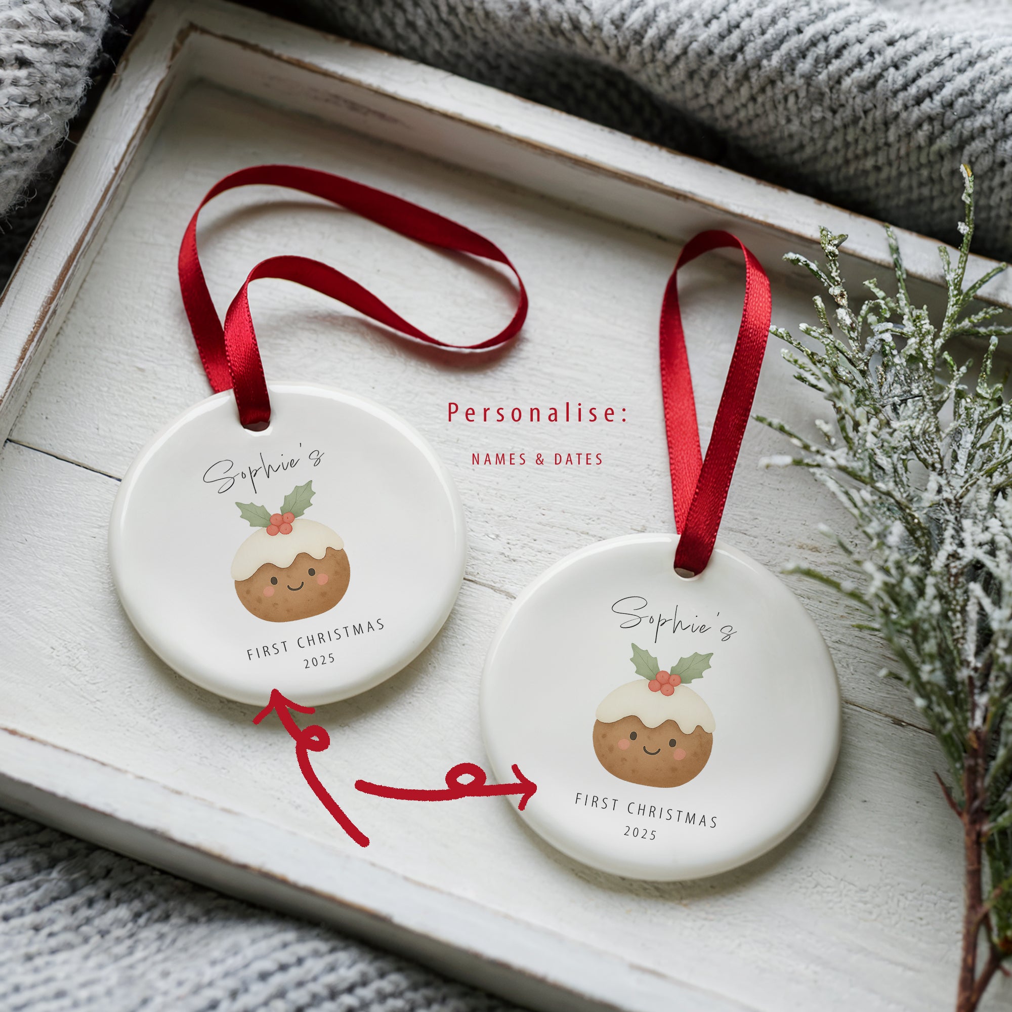 Two personalised baby’s first Christmas pudding ornaments with red ribbons showing custom name and date options, displayed on a white wooden tray with cosy winter textures