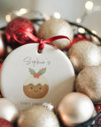 Personalised Christmas pudding baby’s first Christmas ornament nestled in a bowl of festive red and gold baubles with warm fairy lights in the background