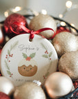 Personalised Christmas pudding ornament with festive holly and pine wreath design, displayed in a bowl of red and gold baubles with warm fairy lights