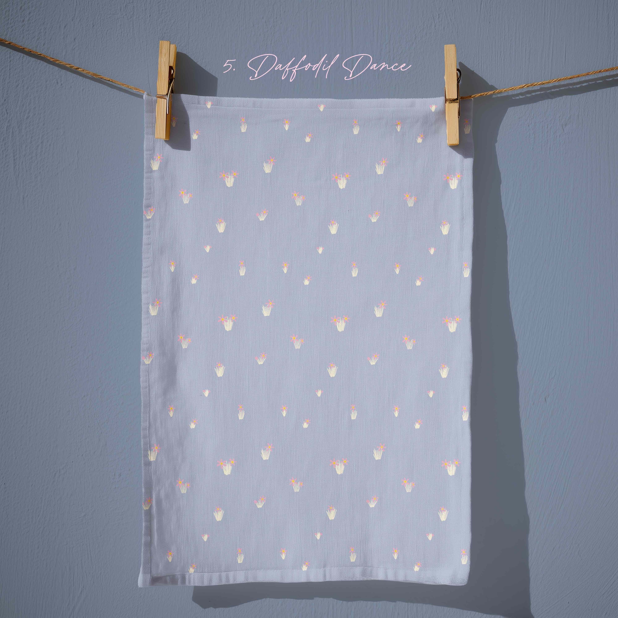Soft powder-blue tea towel featuring small pastel floral sprigs in pink, white and yellow, evenly spaced for a delicate, understated spring pattern.