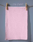 Blush pink tea towel covered in tiny scattered floral stars in lilac and rose tones, creating a sweet, ditsy spring pattern with vintage charm.