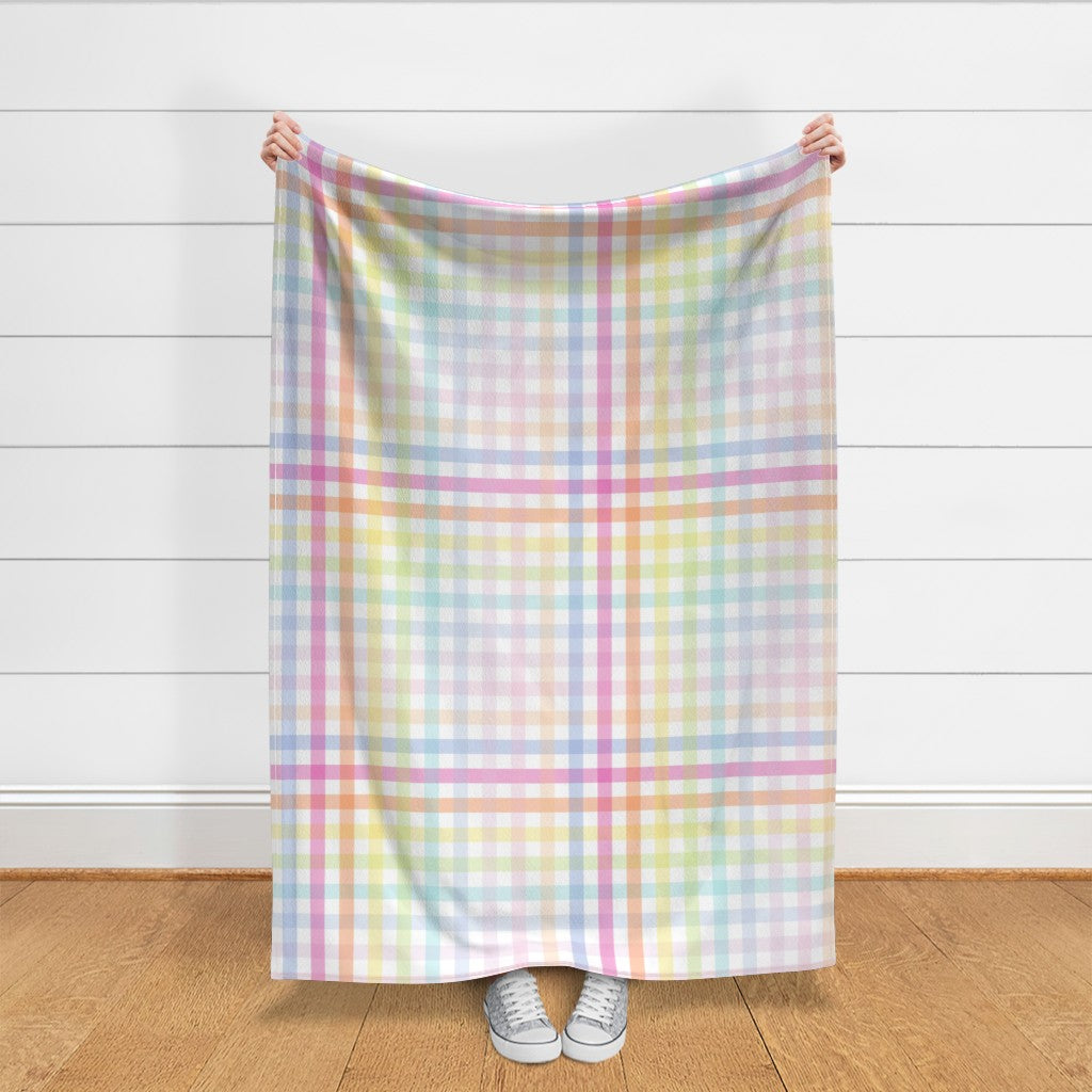 Length of large scale pastel rainbow gingham fabric held against a white shiplap wall, showing the soft pink, blue, lilac, mint and peach check.