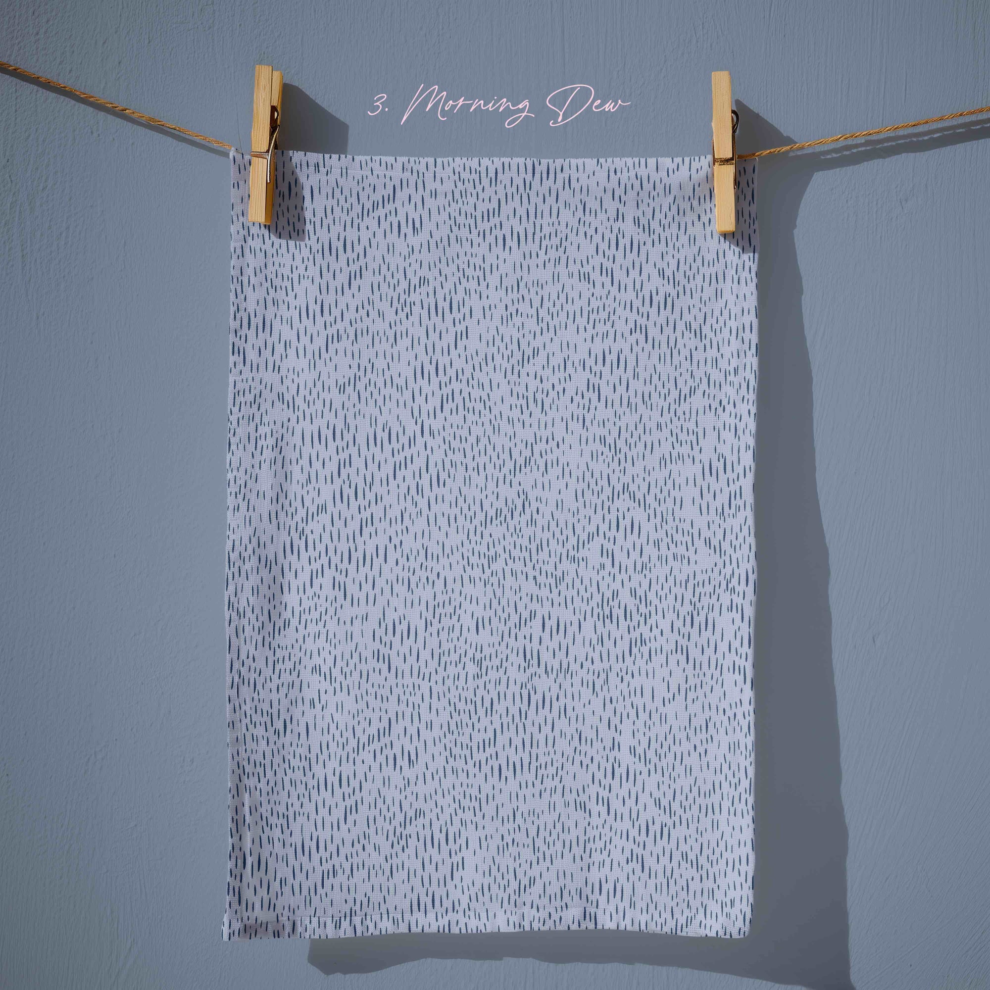 Powder blue tea towel with fine navy dash markings scattered across the surface, creating a subtle dew on grass texture with a calm, minimalist spring aesthetic.