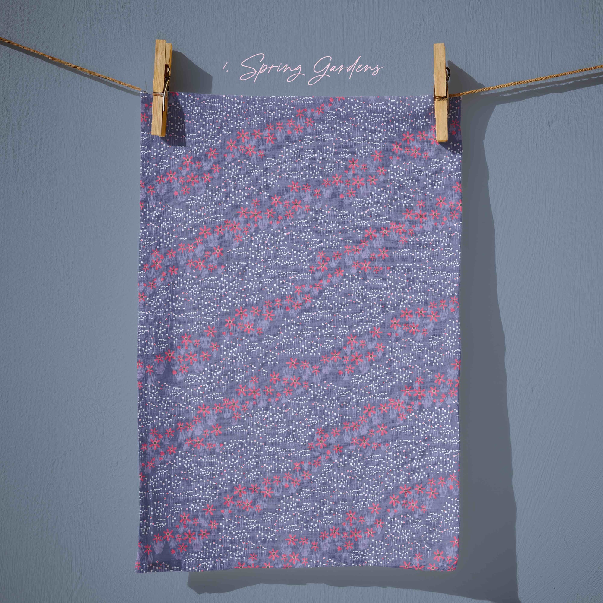 Blue tea towel with flowing trails of small pink blossoms and scattered white crocus speckles, creating a soft dusk-inspired floral pattern with gentle movement and layered texture.